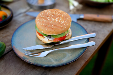 Close up of plate with homemade grilled hamburger and cutlery. Summer outdoor barbecue.