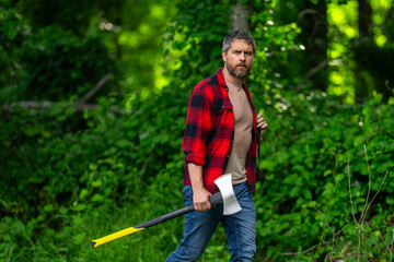 Handsome man or lumberjack in checkered shirt hold axe. Lumberjack or woodman. Masculinity concept. Man brutal strong attractive guy cutting wood with axe in forest. Lumberjack with big axe in forest.
