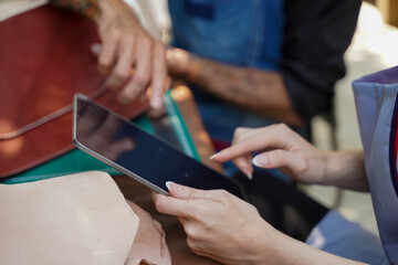 Closeup hands of young female leather maker with craftsman to check the leather rolls in the stock with tablet in the workshop.