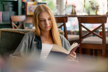 close up in a beautiful bookstore a young girl with long hair sitting in a chair reads a book...