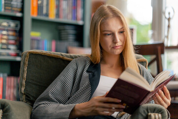 close up in a beautiful bookstore a young girl with long hair sitting in a chair reads a book...