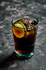 Glass of rum and coke on a wooden table with ice cubes and lime wedges.