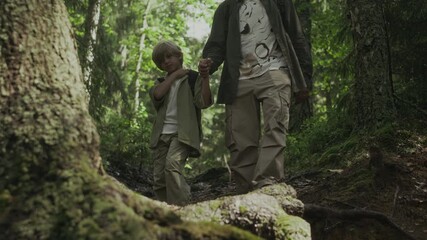 Full shot of Caucasian father and son holding hands while walking on rough path in summer forest
