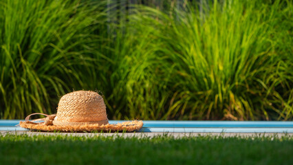 Straw hat lying on the edge of the pool with green grass in the background
