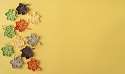 Group of crocheted leaves in different colors on a yellow background. Copy space