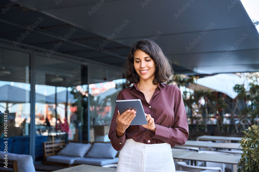 Wall mural Young latin Hispanic adult professional business woman looking at online trade app. European mature businesswoman CEO holding digital tablet using fintech tab application working in workspace office