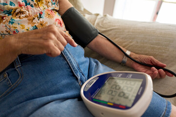 Unrecognizable Senior woman measuring her blood pressure at home. Hispanic Senior Woman Measuring Blood Pressure at Home Using Digital Monitor for Healthcare and Wellness.