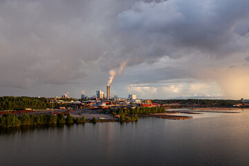 Industrial landscape with lake, stormy sky and factory during golden hour. Industry harmonized with nature concept