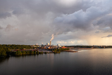 Industrial landscape with lake, stormy sky and factory during golden hour. Industry harmonized with nature concept