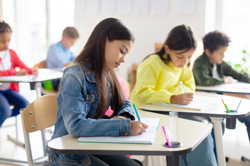 Smart European school children sitting at desks, studying in classroom and writing in their copybooks, creating studious atmosphere