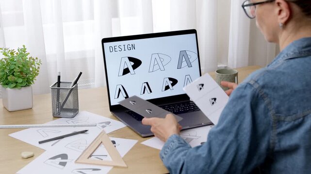 Female artist developing a logo. Sketches of brand designs on a laptop monitor screen.