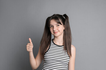 Portrait of cute teenage girl showing thumbs up on grey background