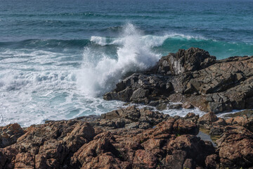 A big wave smashes into a large rock formation and breaks over it at the mouth of a small inlet at Hastings Point, a popular tourist destination in New South Wales, Australia.