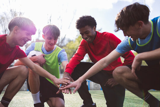 Happy soccer team stacking hands together on field