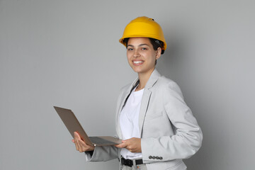 Engineer in hard hat with laptop on grey background