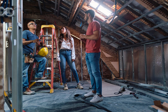 Man and woman having discussion with construction worker in attic at construction site