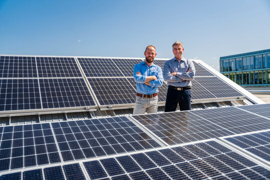 Two businessmen exude confidence as they stand among rows of solar panels, showcasing their commitment to renewable energy.