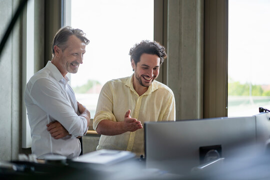 Happy business colleagues discussing near monitor screens at office