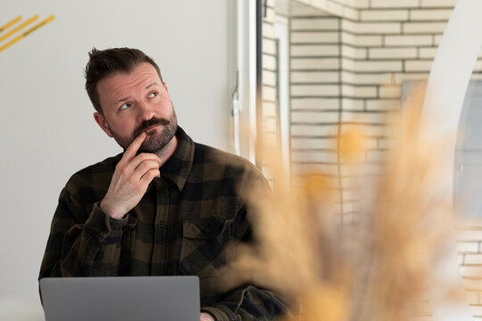 Thoughtful businessman in flannel shirt with laptop at office