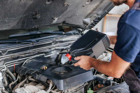 Man pouring liquid in car engine inside garage