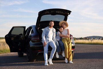 Happy family sitting in trunk of car outdoors