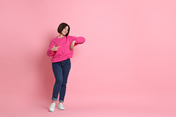 Smiling woman pointing at something on pink background. Space for text