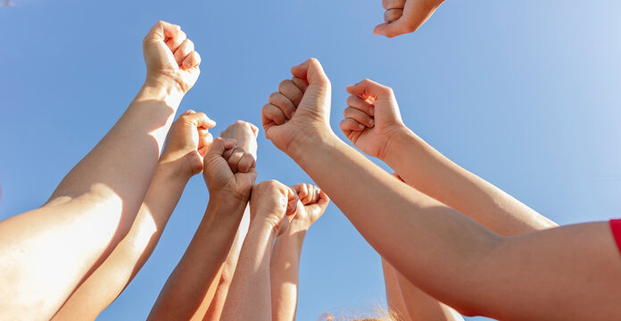 Hands of athletes cheering together under sky on sunny day