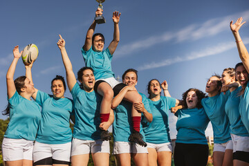 Cheerful rugby players celebrating victory with trophy on sunny day