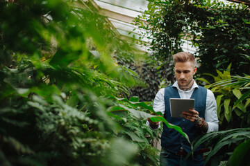 Small greenhouse business. Businessman selling flowers and seedlings, standing in greenhouse,...