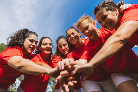 Happy rugby players stacking hands under sky