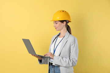 Engineer in hard hat with laptop on yellow background