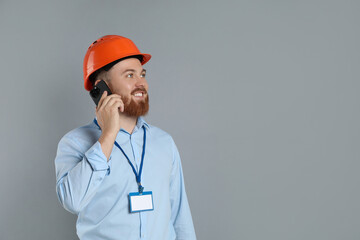 Engineer in hard hat talking on smartphone against grey background, space for text