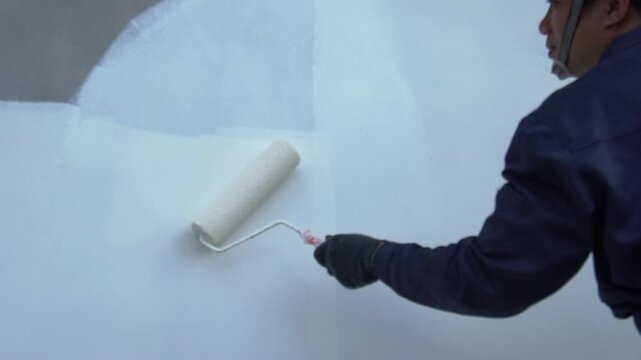 Close up of painter hand holding brush painting white wall. Home painting and decorating concept. House for sale or real estate.