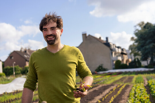 Smiling man holding seedling and standing on farm
