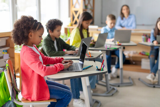 Modern elementary education concept. Group of diverse school children sitting at desks with laptops, studying, using digital gadgets