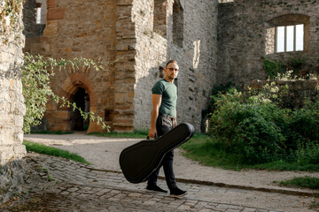 Man holding guitar case and standing near ruins of castle