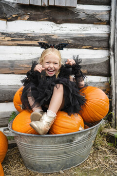 Cute smiling girl sitting over pumpkins in bucket