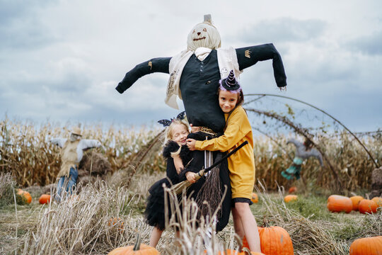 Girls embracing scarecrow in pumpkin patch