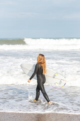 Woman with surfboard walking on wet beach