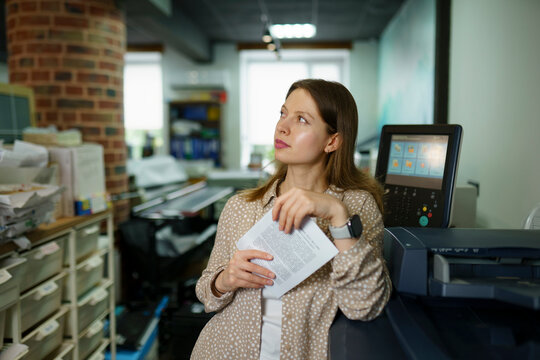 Thoughtful businesswoman holding paper and leaning on photocopier at office