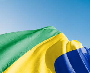 Gabon national flag cloth fabric waving on beautiful sky blue Background.