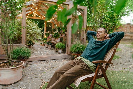 Business owner relaxing on deck chair outside greenhouse in back yard
