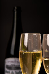 A vertical image of champagne bottle and two glasses brimming with bubbles, on a black background. Ideal for New Year's Eve and festive celebrations.