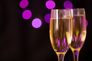 Champagne glasses filled with bubbles, aligned to the right of the image. The background features a black backdrop with blurred violet lights, evoking a festive atmosphere perfect for New Year's Eve.