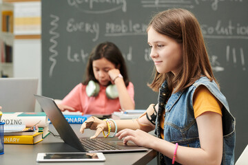 Side view portrait of smiling young girl with prosthetic arm using laptop during IT class for...