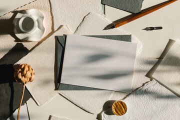 Overhead view of a blank paper card, an envelope, calligraphy tools, a dried flower, and ceramics...