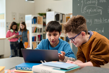 Portrait of two young boys using computer together in colorful school library setting and looking at screen