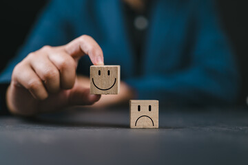 Hand holding smiley happy face on wooden cube and unhappy sad emotion on the floor. World Mental...