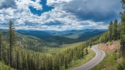Scenic Mountain Road Winding Through Lush Green Forest with Majestic Cloudy Sky and Distant Mountain Range