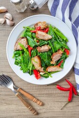 Stir fried Chinese Broccoli with crispy pork,Crispy pork with Chinese broccoli,Stir fried crispy pork in kale in a white plate on wooden background